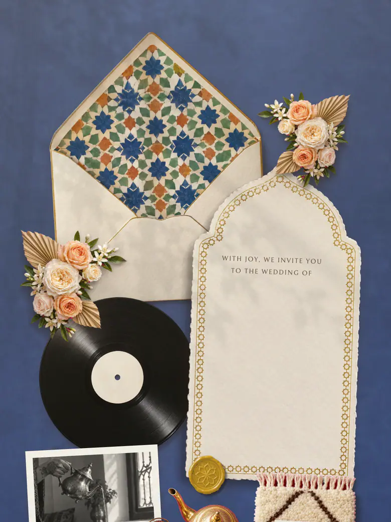 The Riad invitation in Majorelle blue: a zellige-tiled envelope liner, apricot roses, a brass seal and an arched card on blue plaster