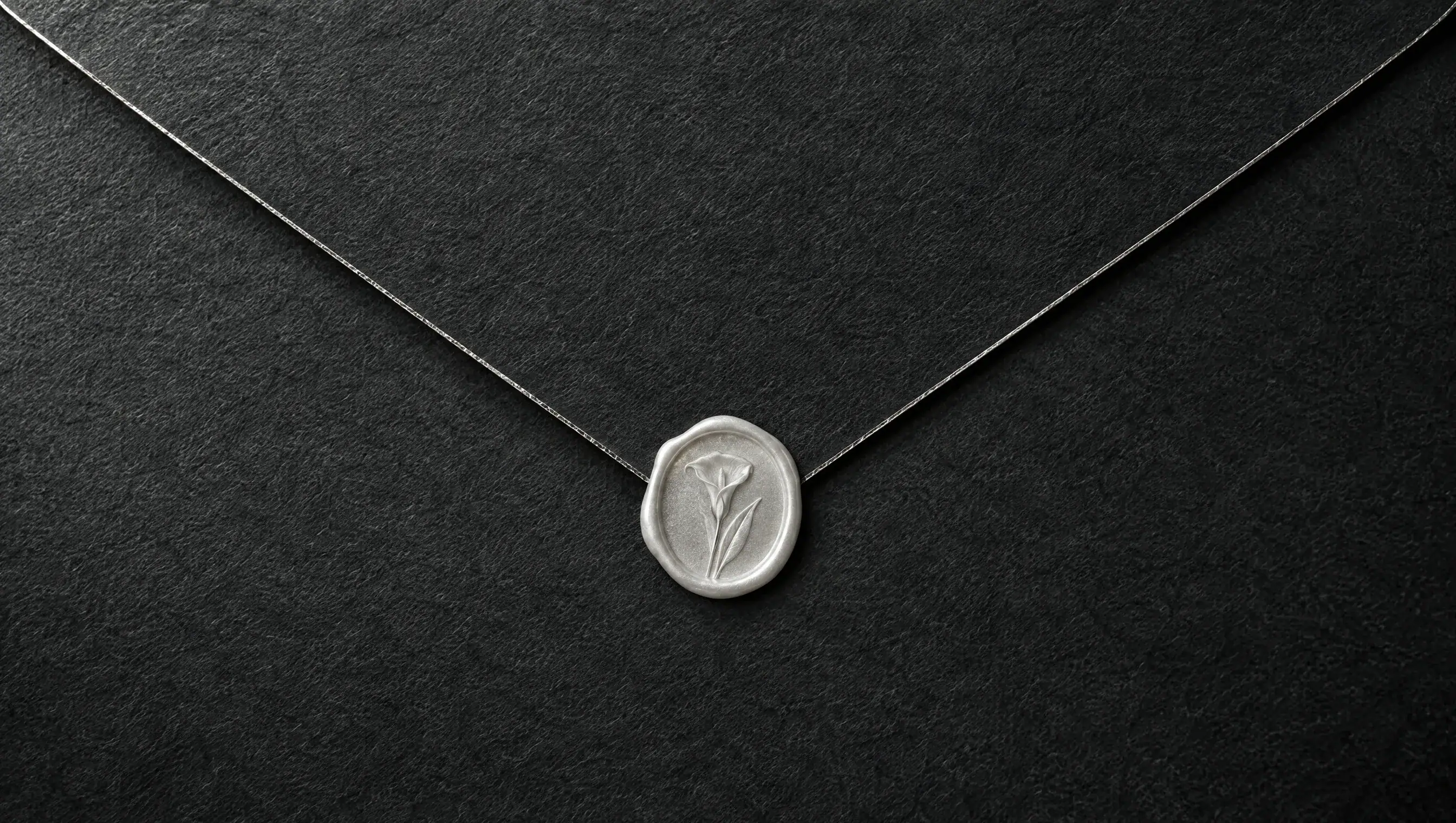 The back of a charcoal-black envelope with a fine silver line along its flap, sealed with pearl-white wax
