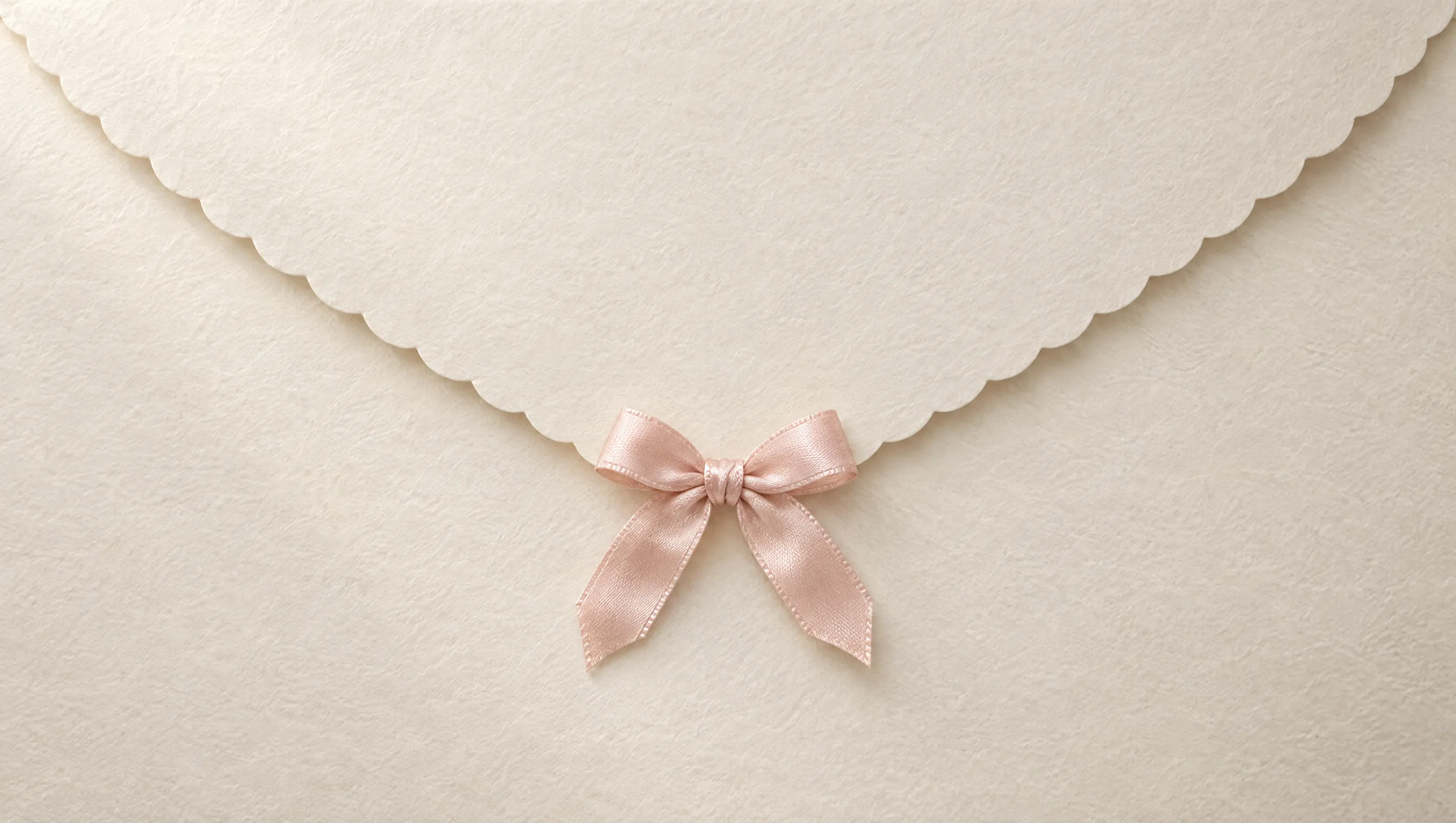 The back of an ivory envelope with a scalloped flap, tied with a blush-pink satin bow