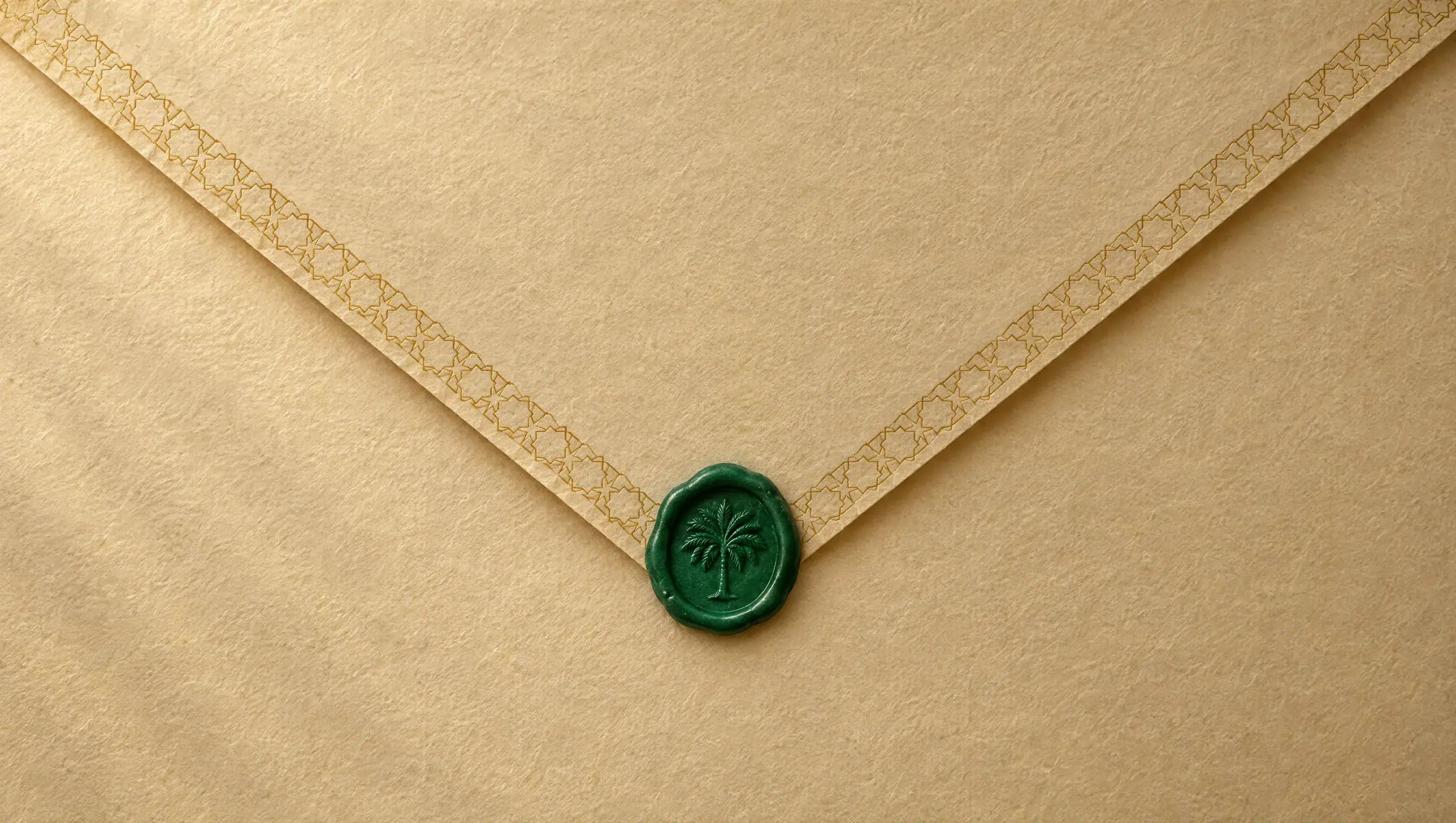 The back of a champagne envelope with a gold geometric border along its flap, sealed with emerald-green wax